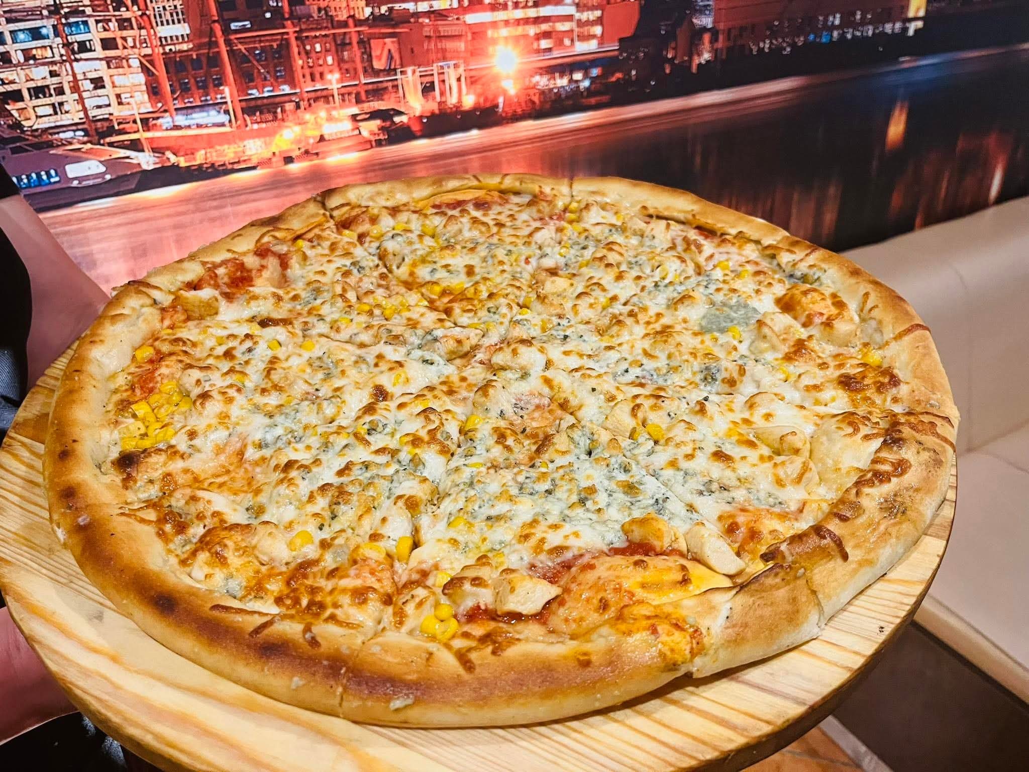 Pizza s kuracím mäsom, kukuricou a syrom na drevenom tanieri